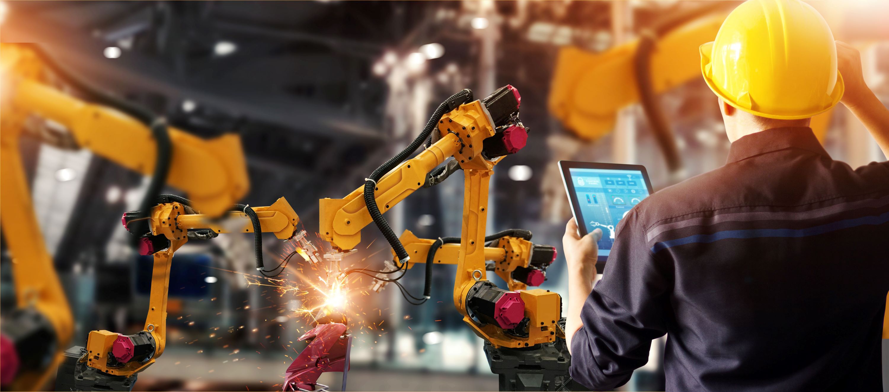 Worker operating two robotic welding arms.