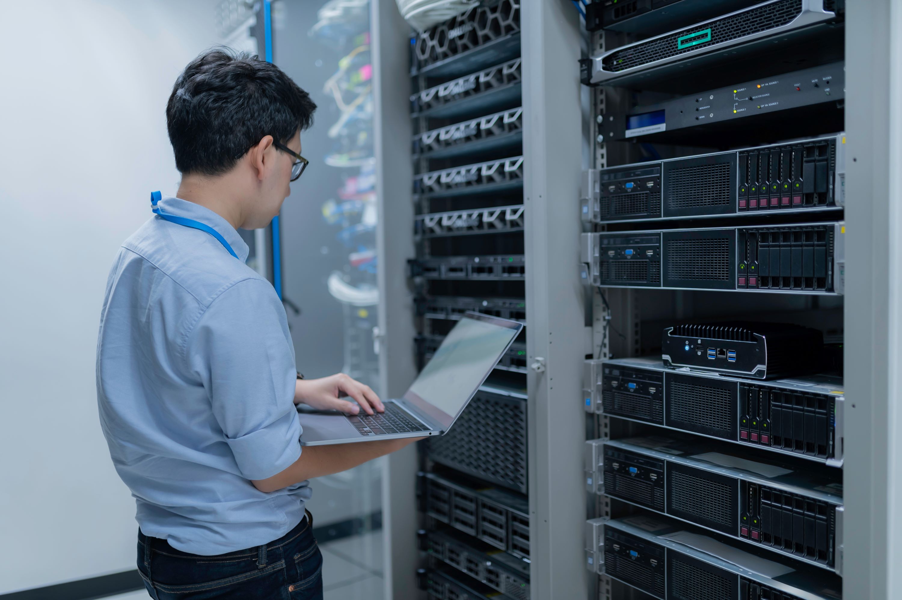Computer professional holding a laptop computer while standing at a server.