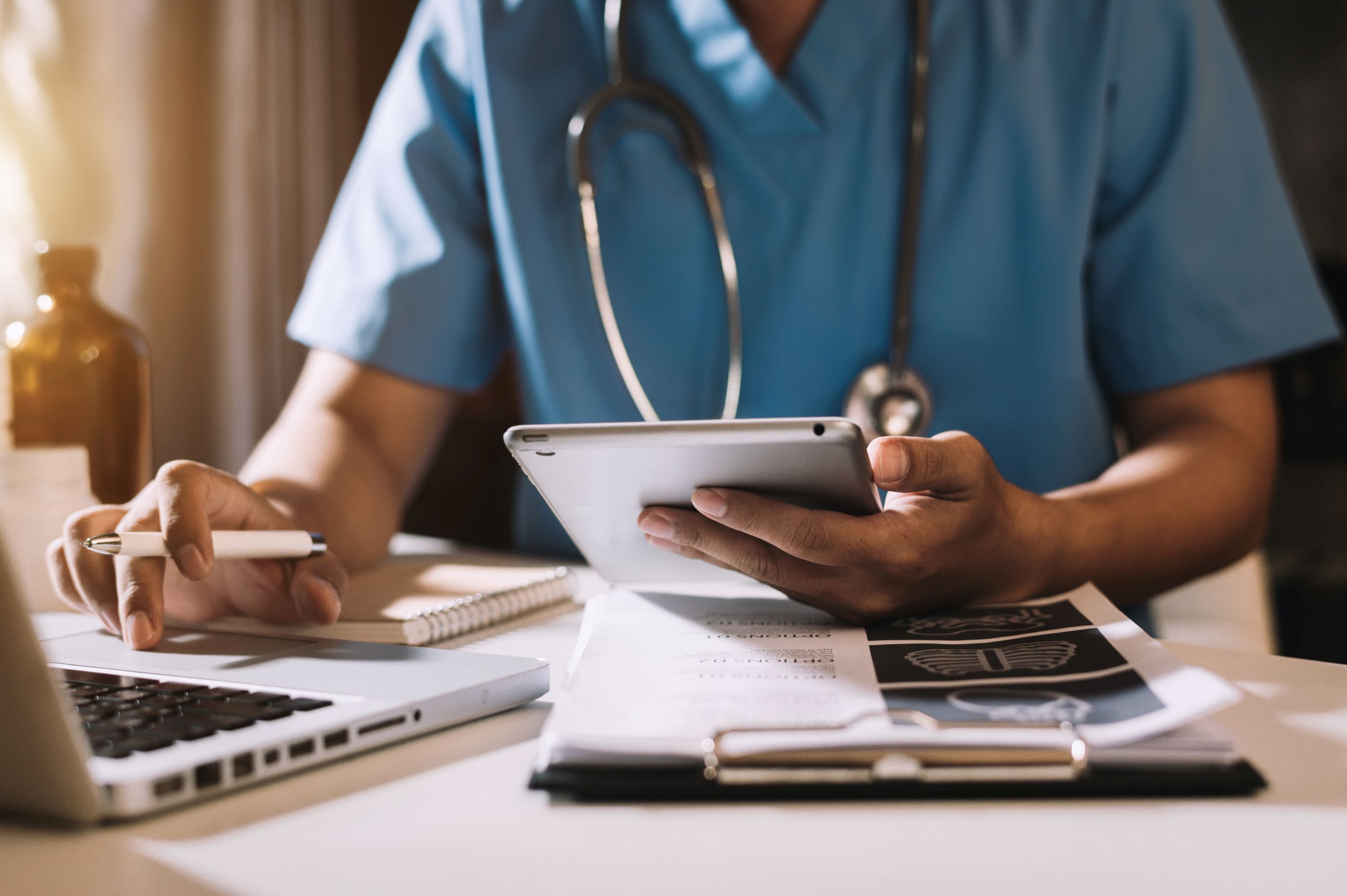 Healthcare professional using a laptop computer and pad device