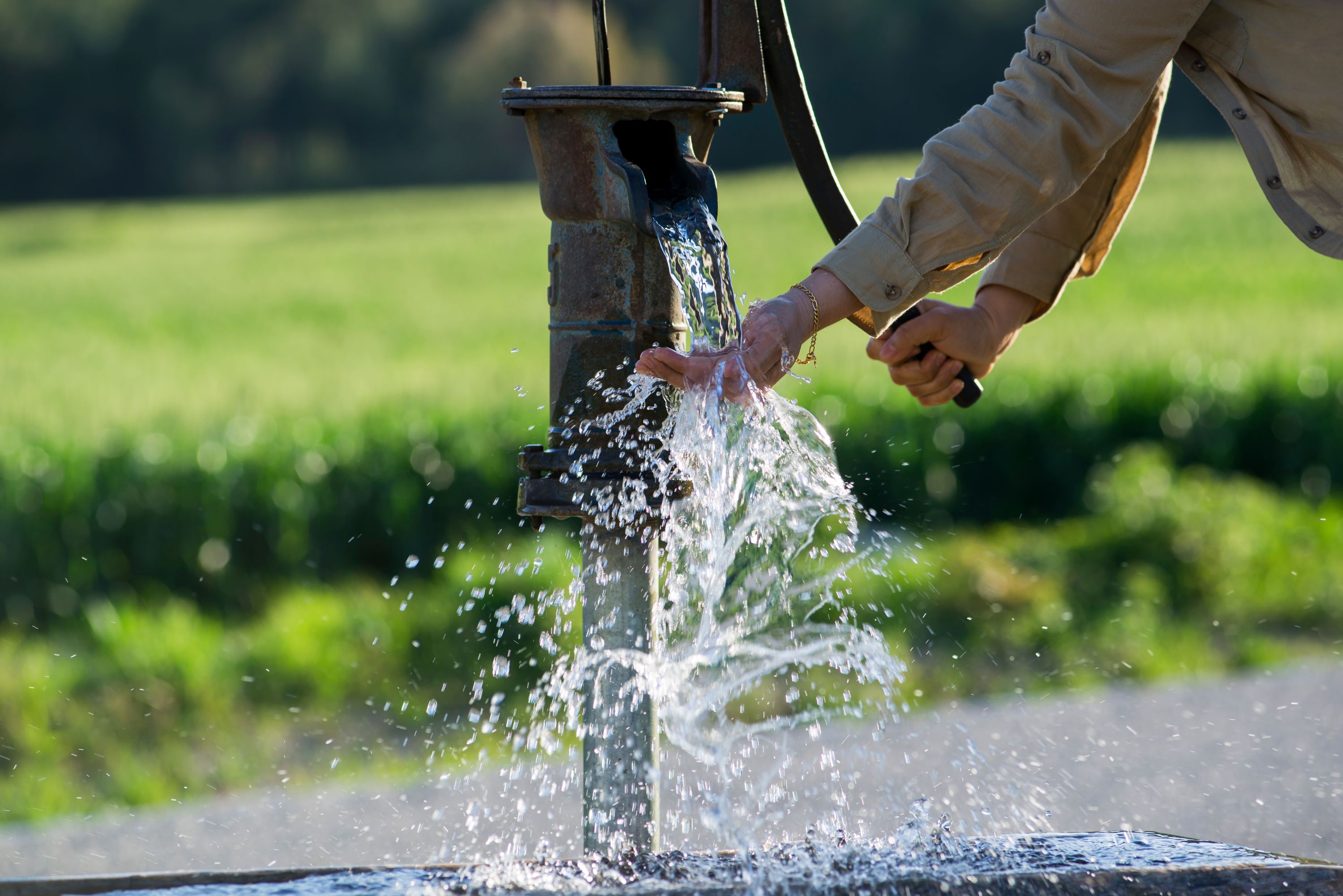 Person using a hand-pump to dispense water from a well.