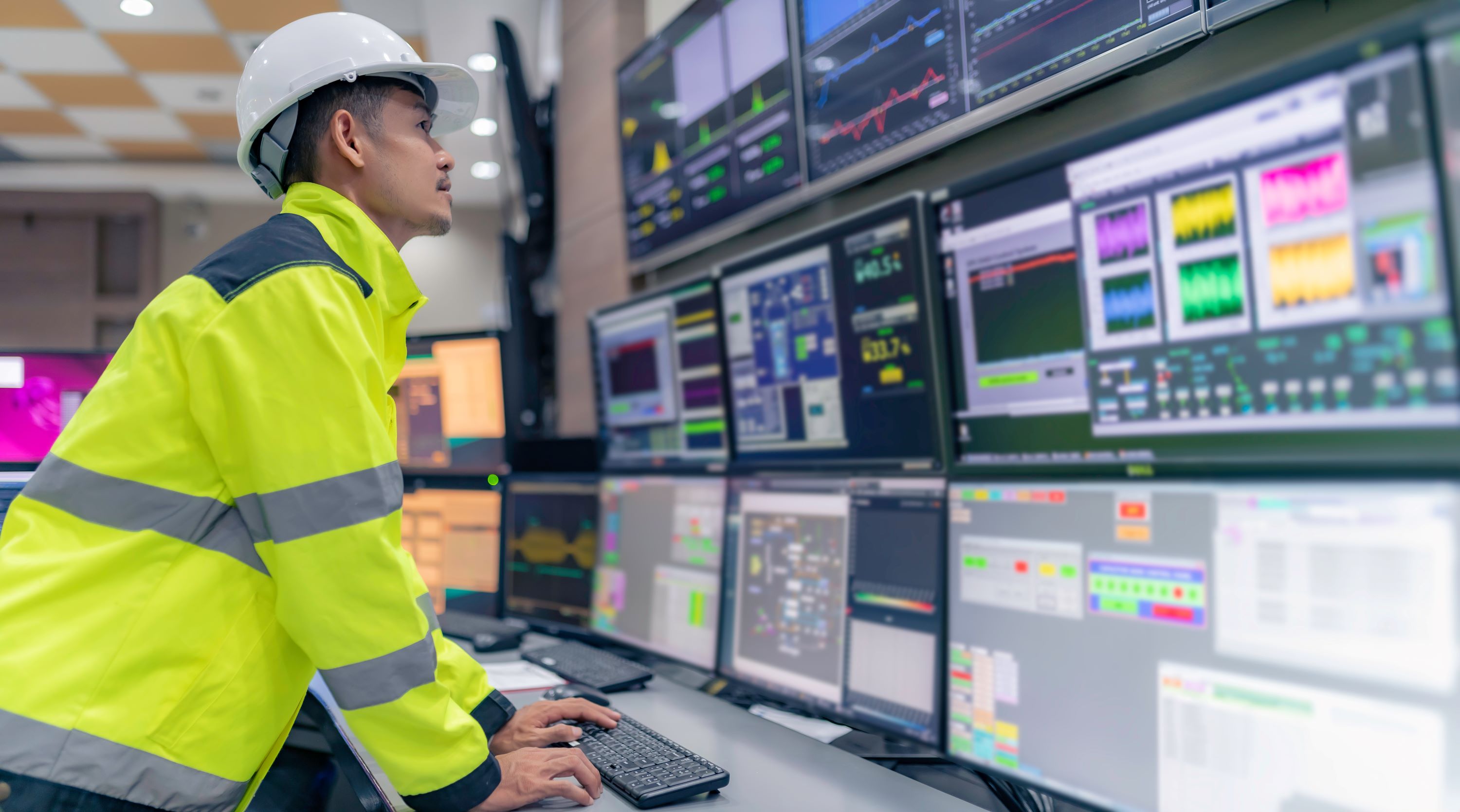 Energy worker standing at a control center with multiple computer monitors.